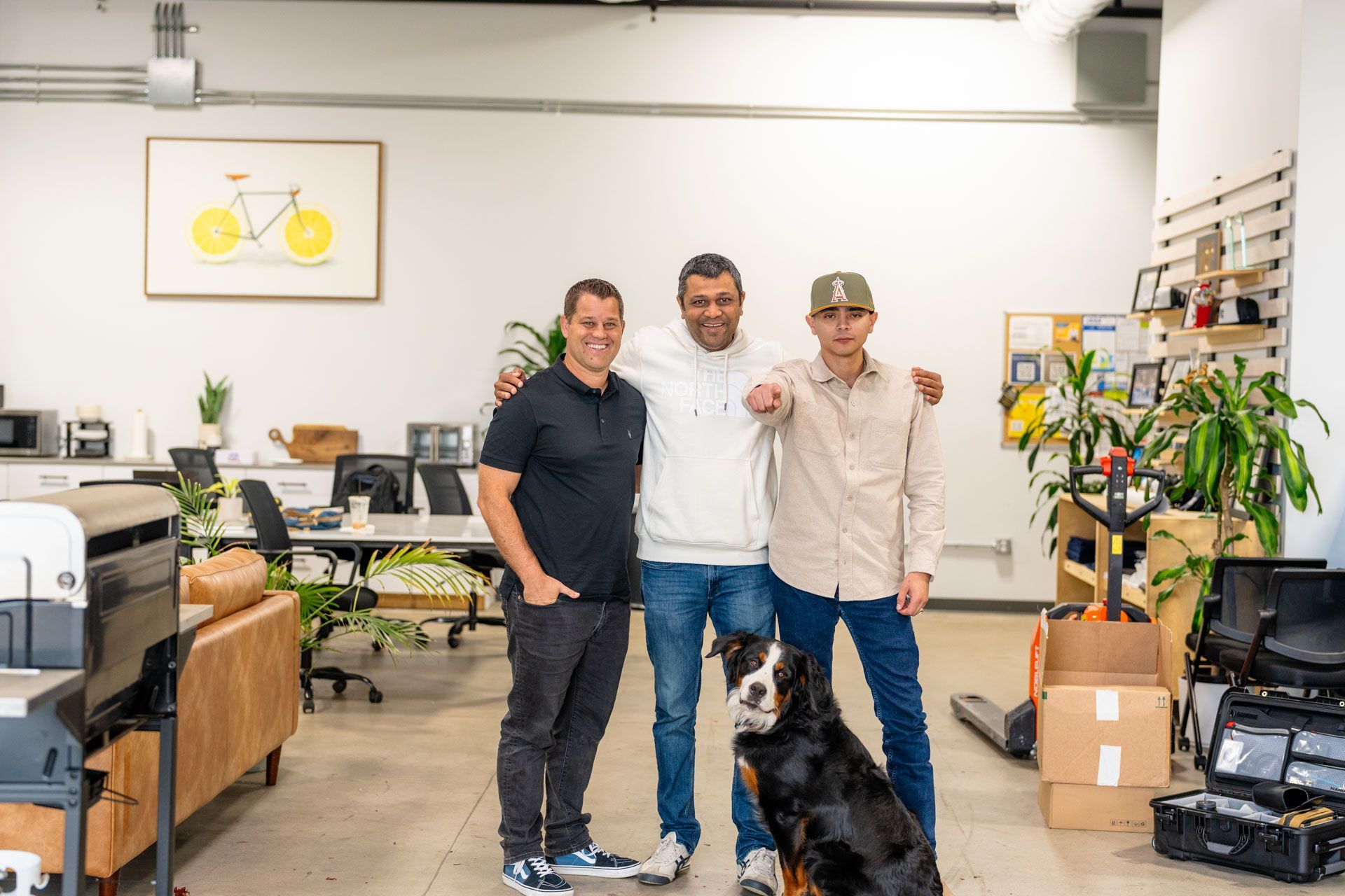 Three people and a dog in a bright office or studio space, posing together and smiling