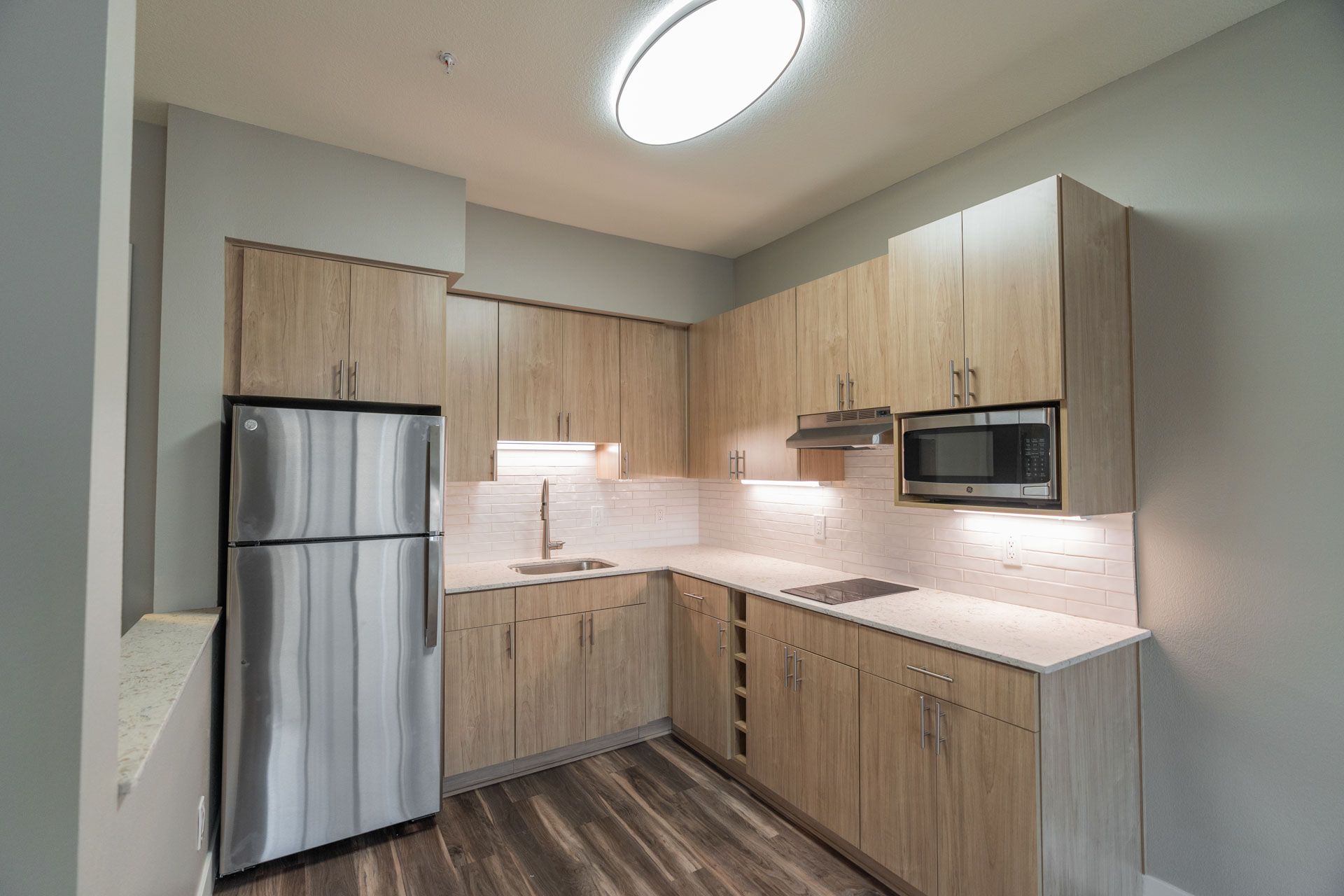 Modern kitchen with stainless steel fridge, light wood cabinets, and built-in microwave under bright ceiling light