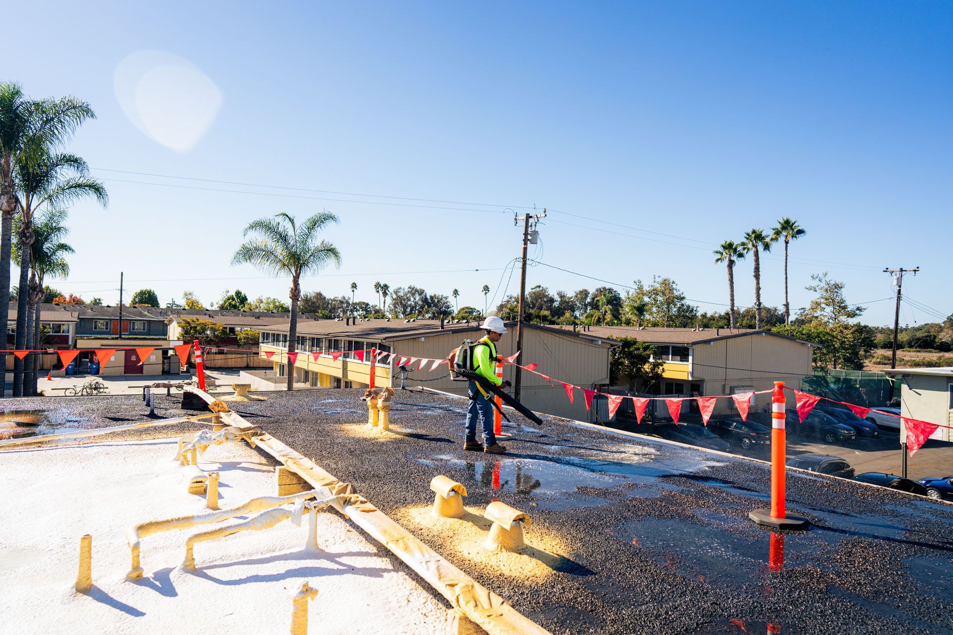 Road construction site with workers, orange cones, and wet pavement under a sunny sky