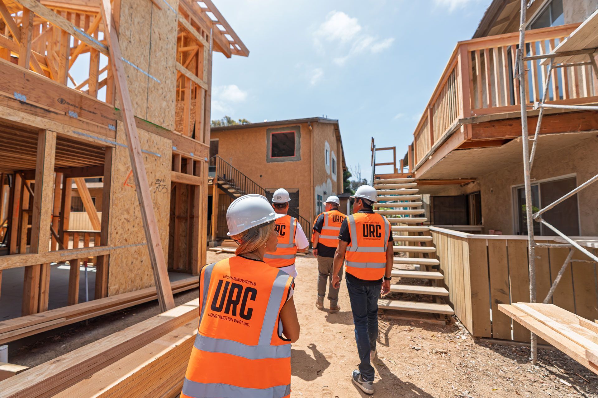 Construction workers in orange vests on a wooden framing site between unfinished buildings