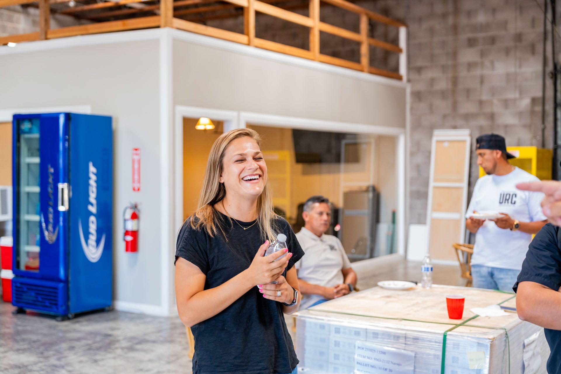 Woman laughing in an indoor warehouse space with vending machines and people in the background
