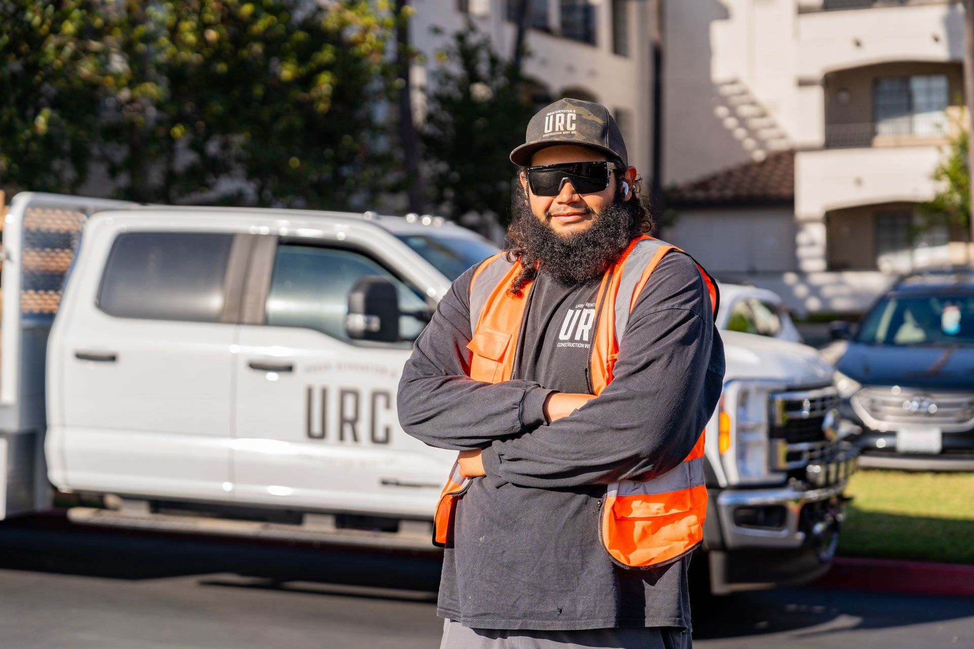 Person in orange safety vest and cap stands in front of a white utility truck outdoors.