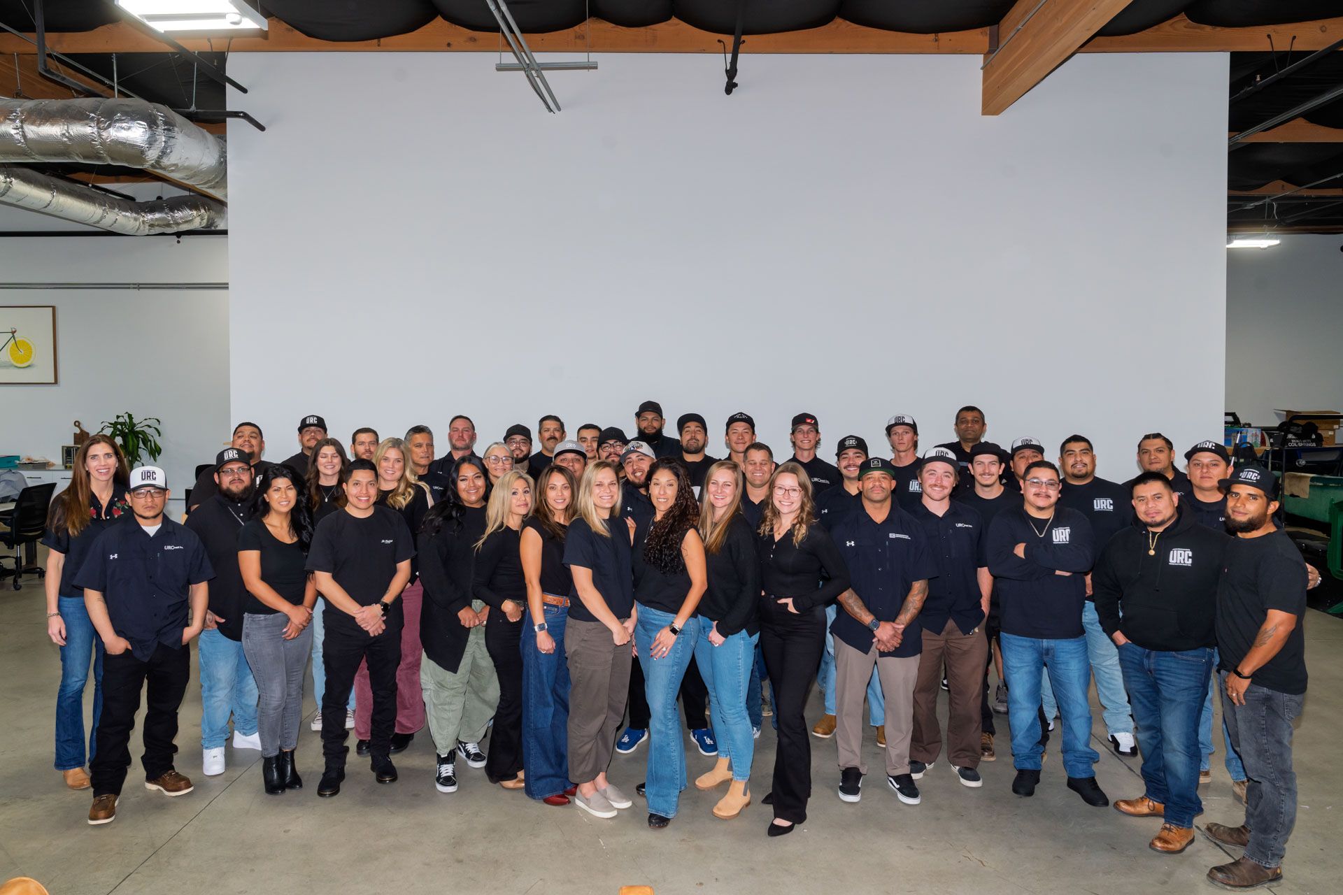 Large group posing indoors in matching dark shirts and jeans in front of a white screen