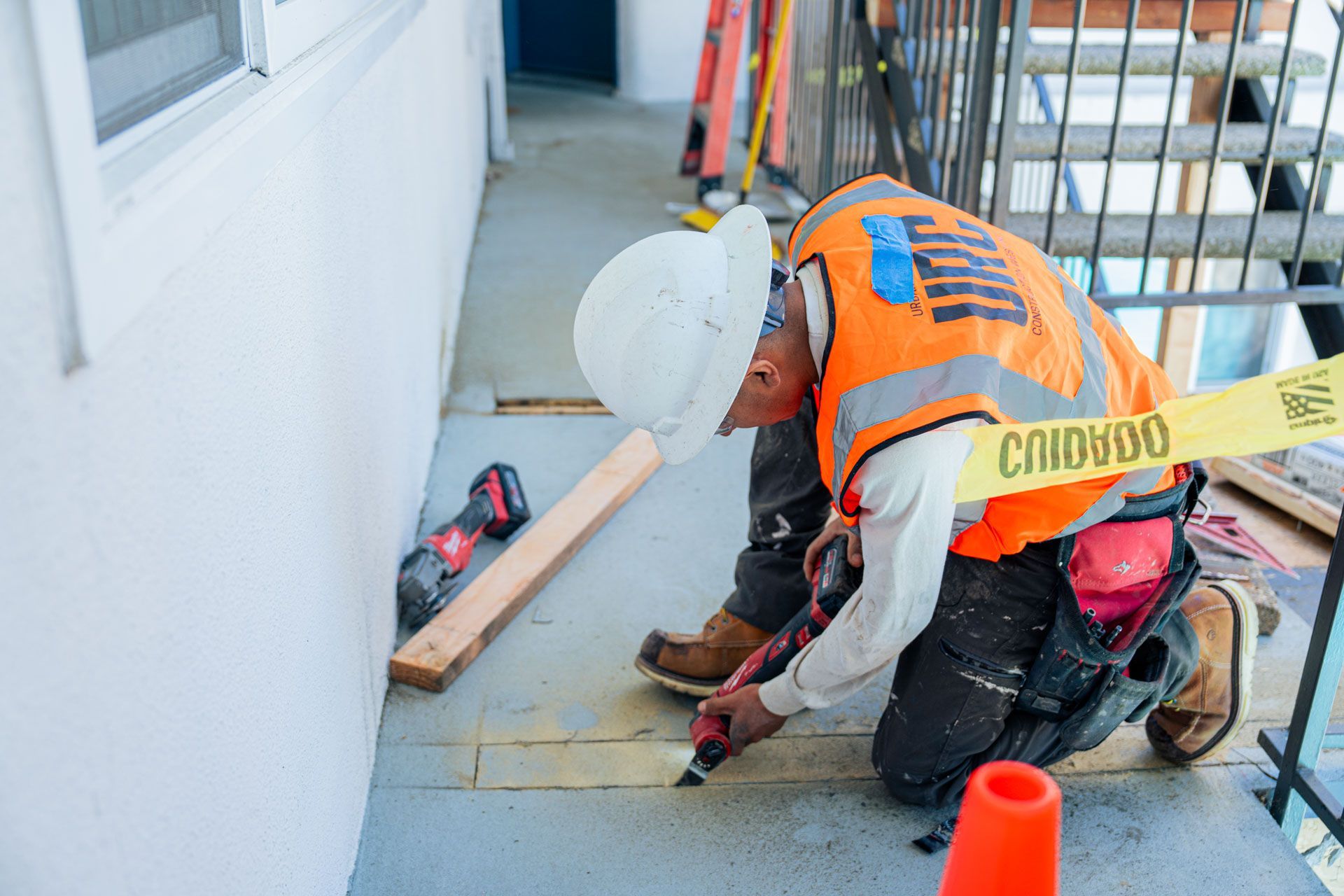 Construction worker kneeling on balcony floor, measuring and marking tiles near a wall and orange cone