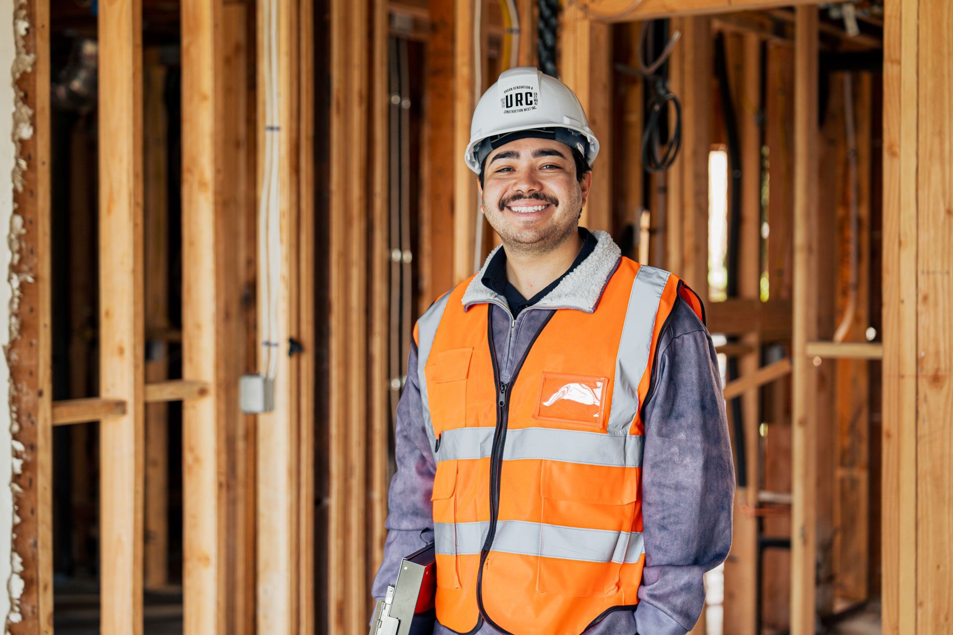 Construction worker in orange safety vest and hard hat smiling at a building site frame