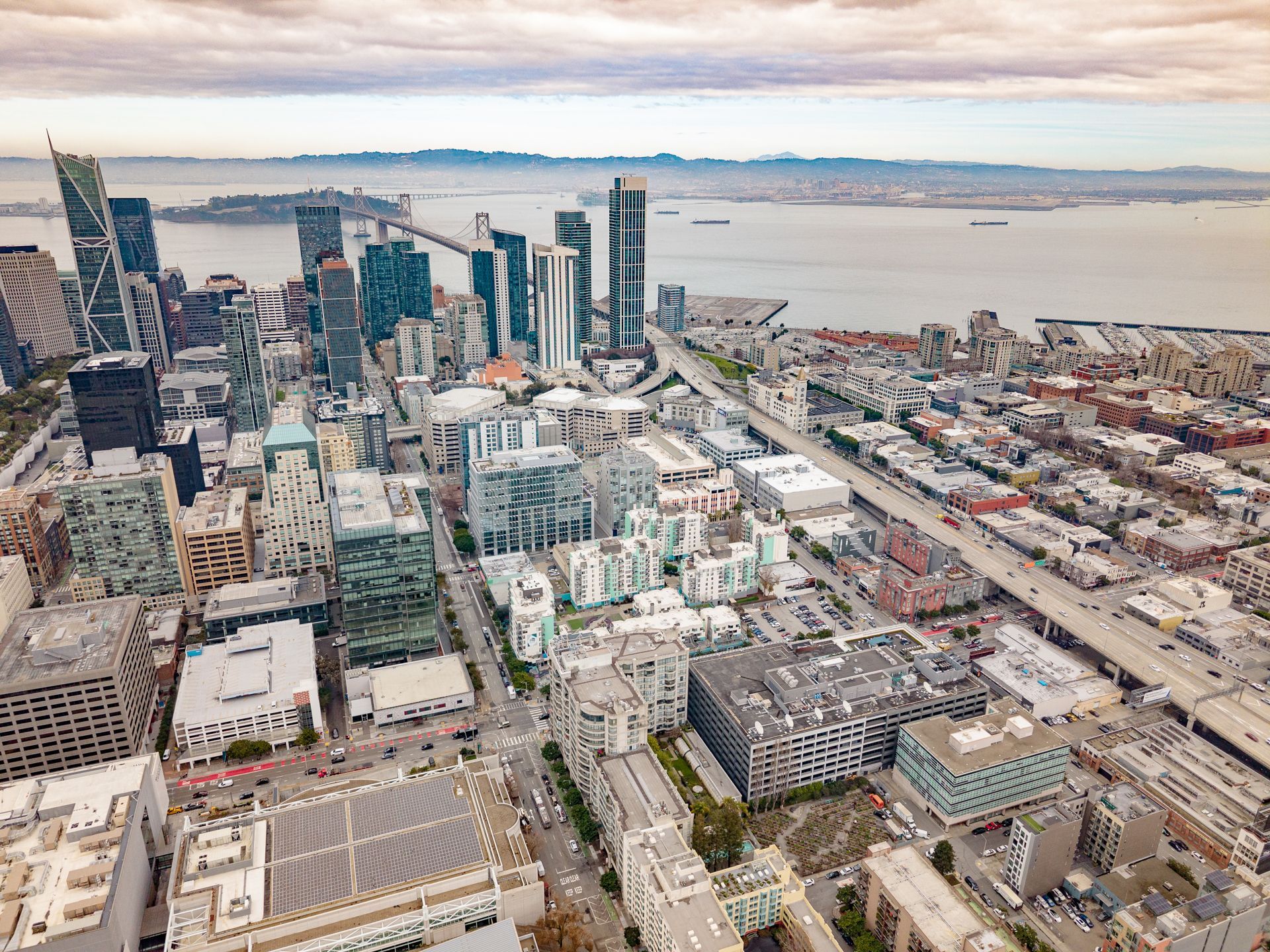 Aerial view of a coastal city skyline with high-rises, roads, and waterfront beyond.