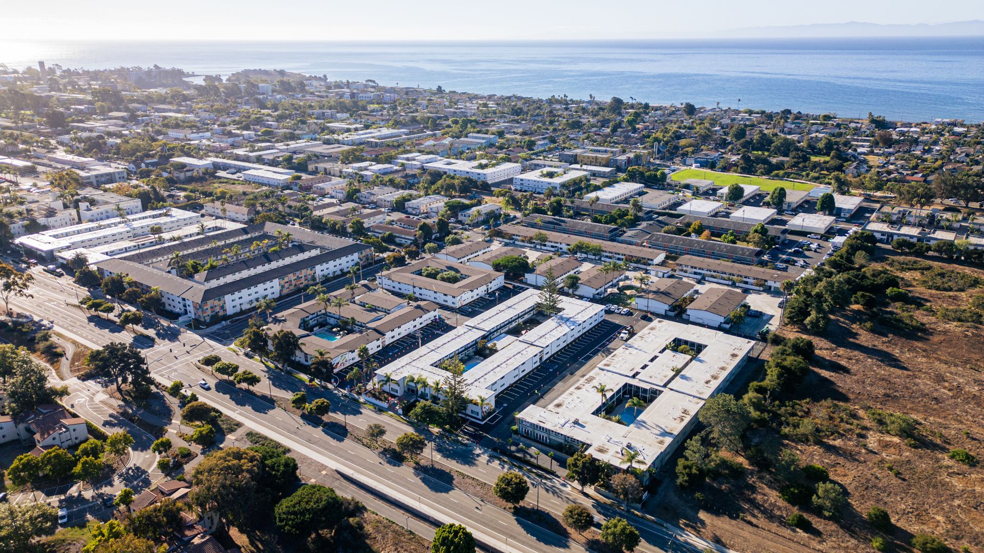 Aerial view of a coastal neighborhood with buildings, roads, and the ocean in the background.