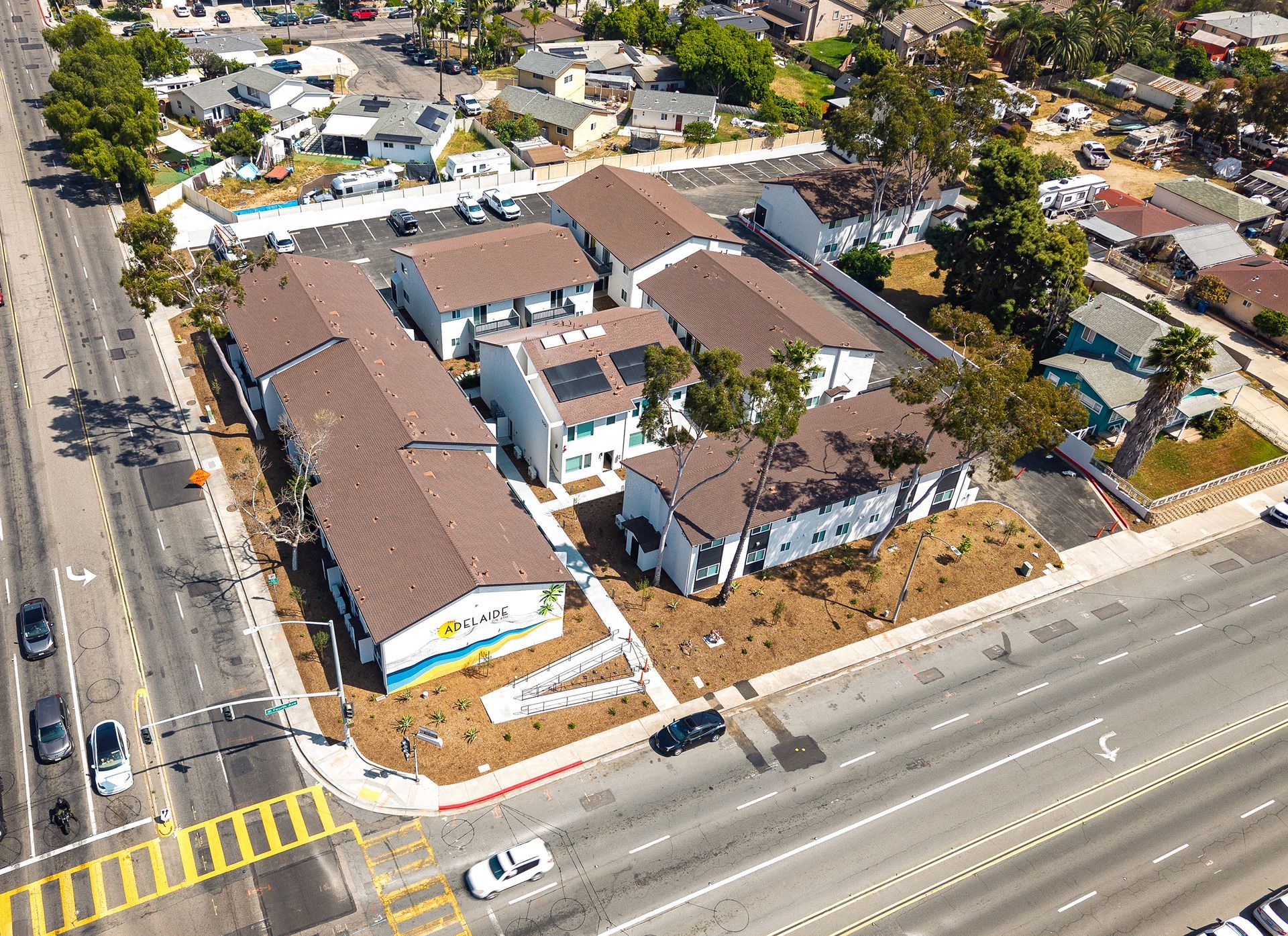 Aerial view of a large brown-roofed building complex beside a busy road in a suburban neighborhood.