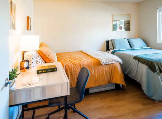 Small bedroom with two beds, a desk, a chair, and a window with soft natural light.