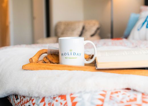 White mug and notebook on a bed with a woven tray in a cozy bedroom scene