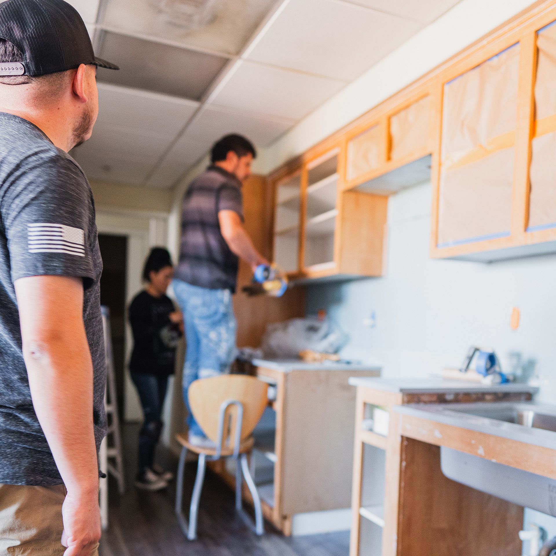 A man with an american flag on his shirt is standing in a kitchen