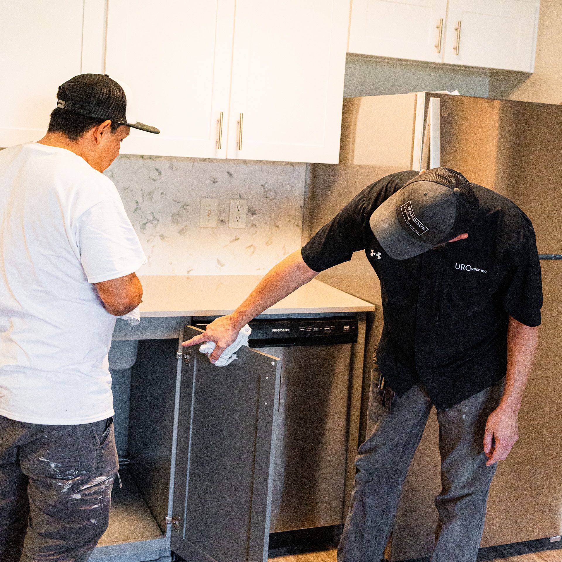 Two men are working in a kitchen and one of them is wearing a hat with the letter h on it