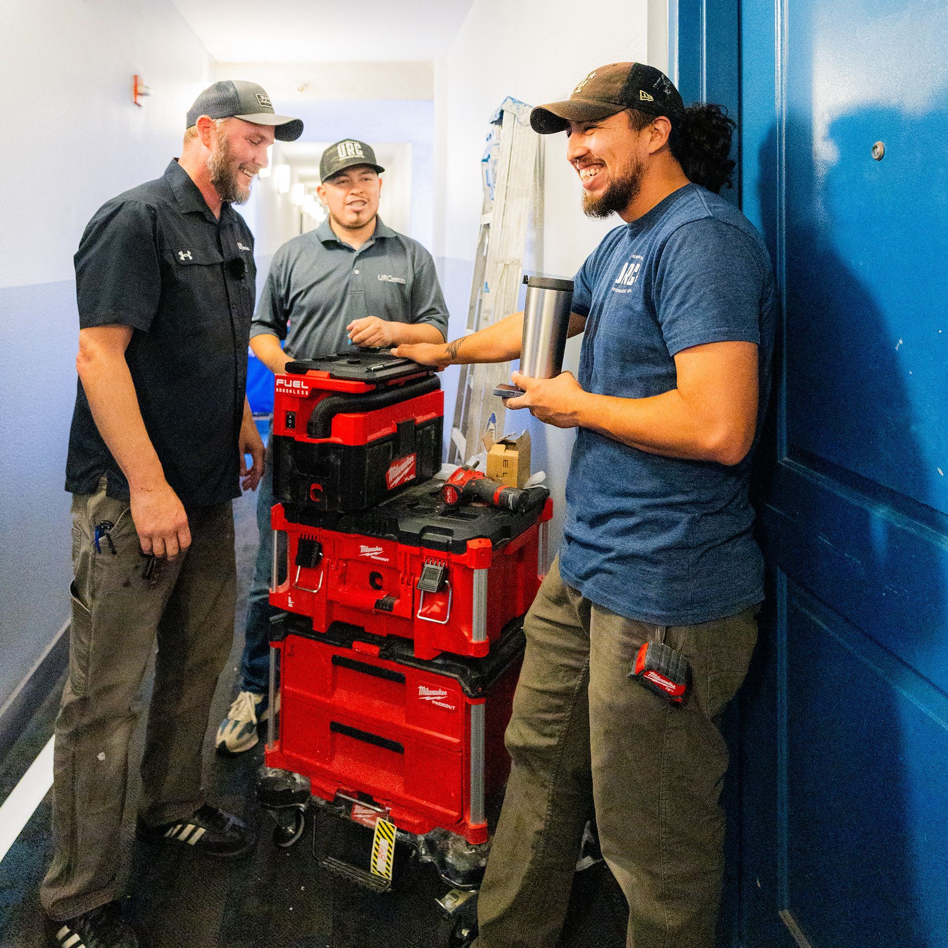 Three men are standing in a hallway talking to each other