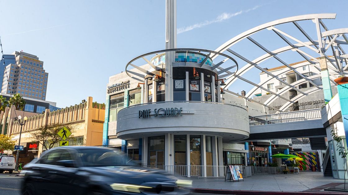 Street corner with a white modern building and curved canopy, cars passing in front.