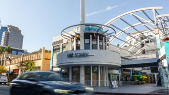 Street corner with a white modern building and curved canopy, cars passing in front.