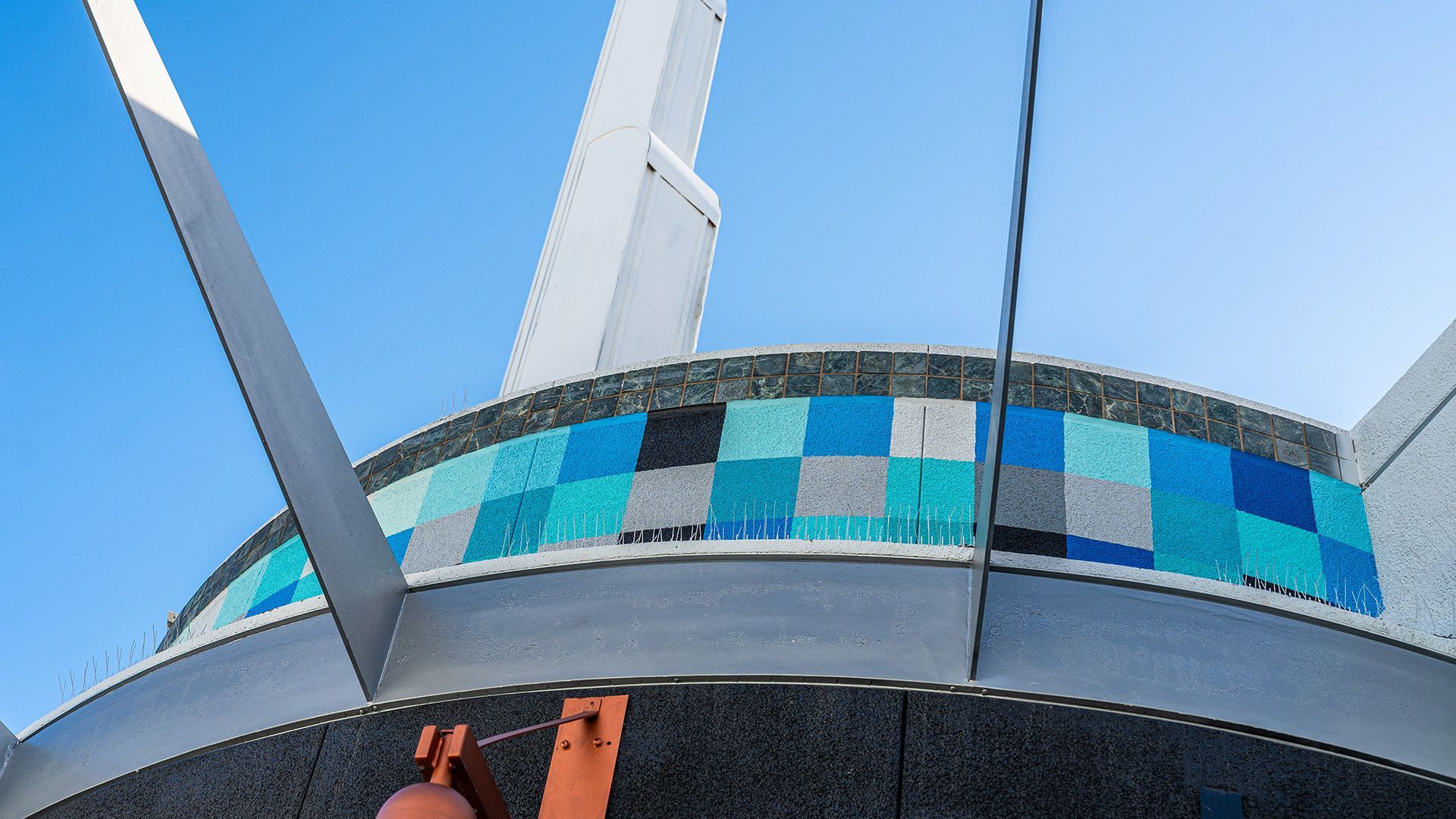 Blue-tiled curved building facade with tall white supports against a clear sky
