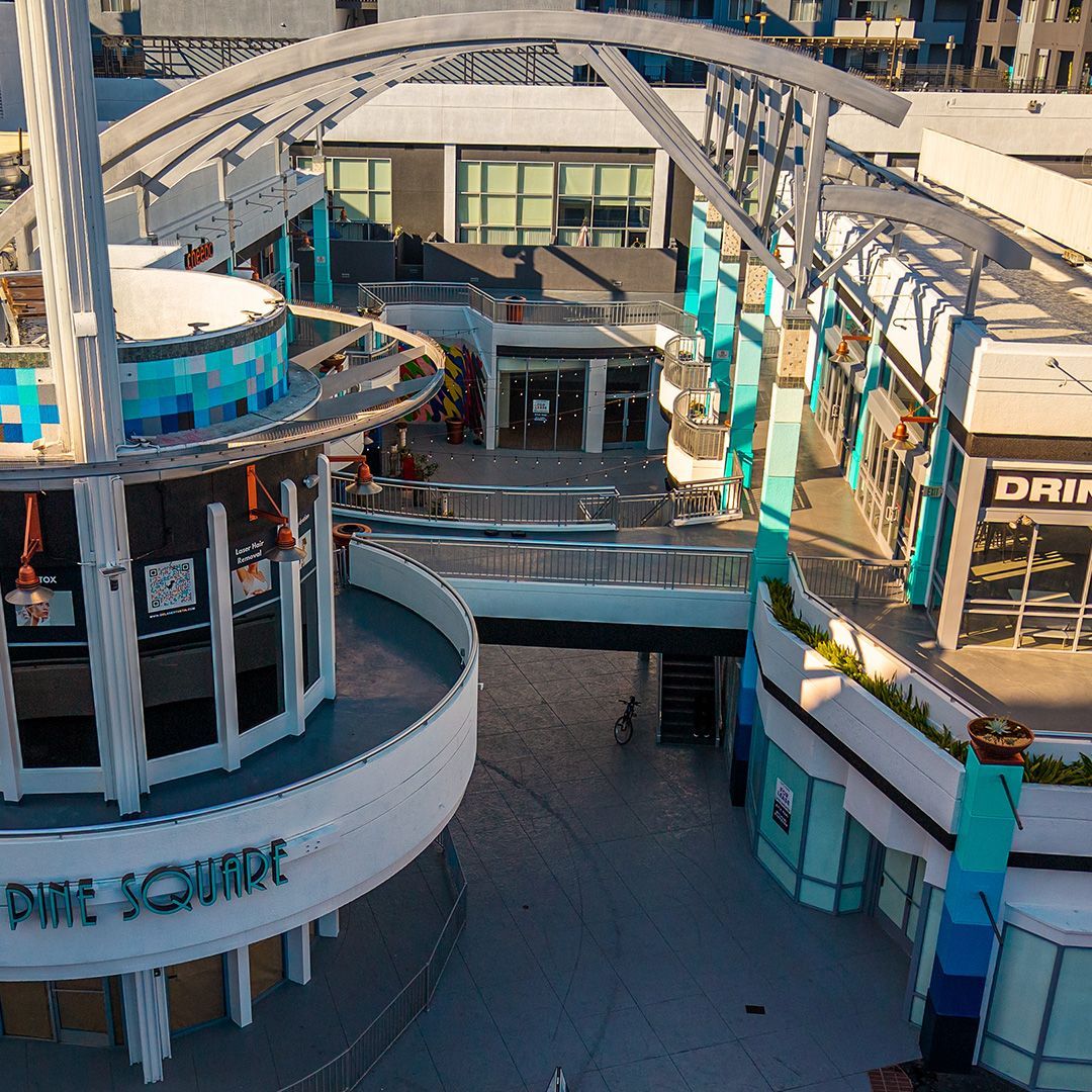Empty outdoor shopping plaza with curved white buildings, blue accents, and overhead arching structures
