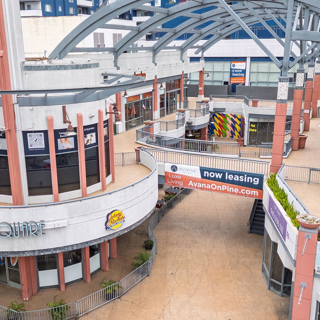 Empty shopping center atrium with storefronts, arched glass roof, and “now leasing” banner