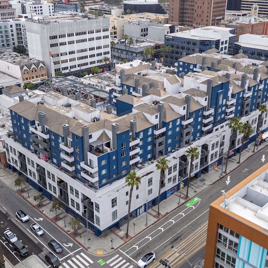 Aerial view of a multi-story building with blue and white facades, palm trees, and street traffic.