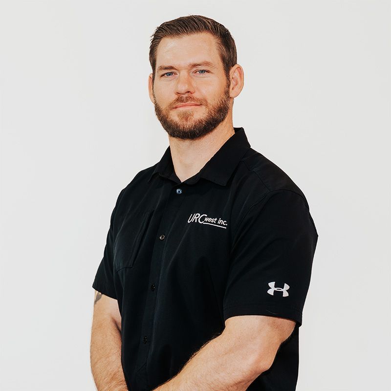 Man in a black polo shirt standing against a white background, arms crossed, slight smile.