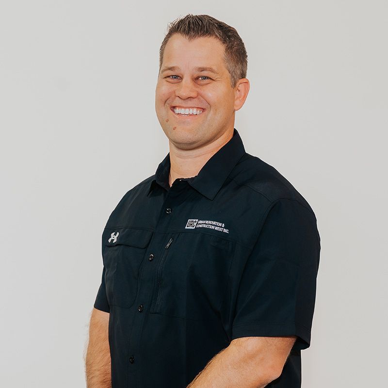 Man standing against a plain background, wearing a black button-up shirt and jeans.
