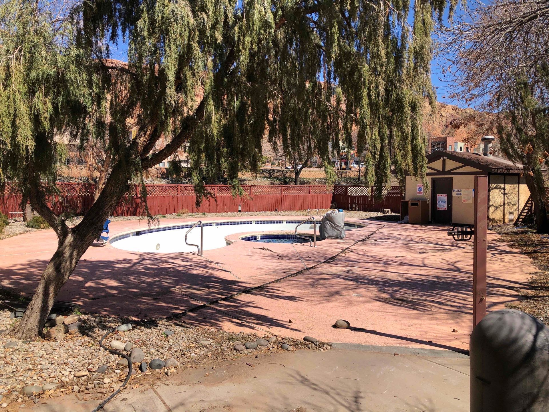A large swimming pool is surrounded by trees and a fence.