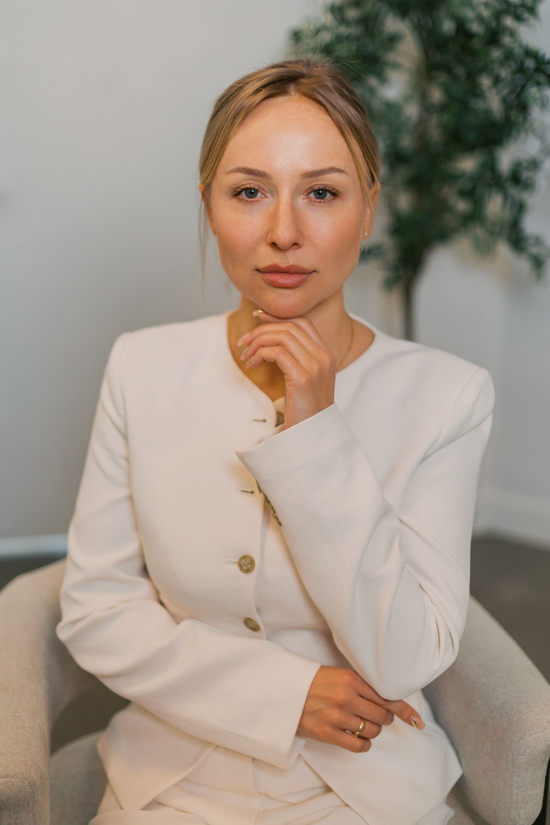Person in a white blazer seated indoors, resting their chin on their hand with a thoughtful expression.