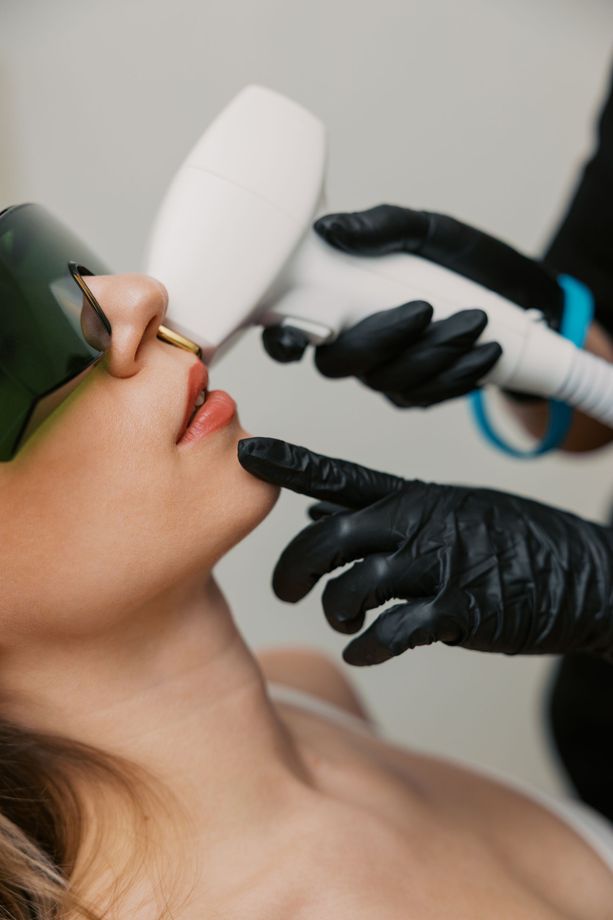 Gloved hands perform facial laser treatment on a patient wearing protective eyewear and a nose ring