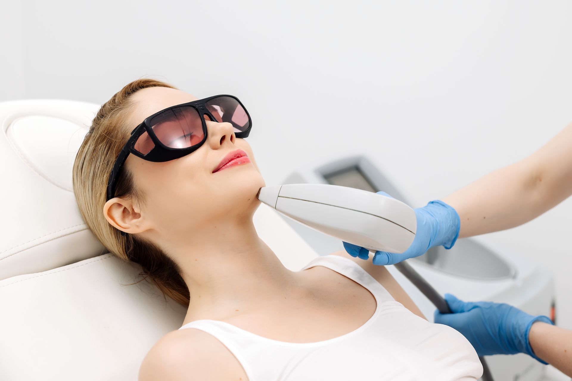Woman wearing sunglasses receives a facial treatment with a handheld device in a spa clinic