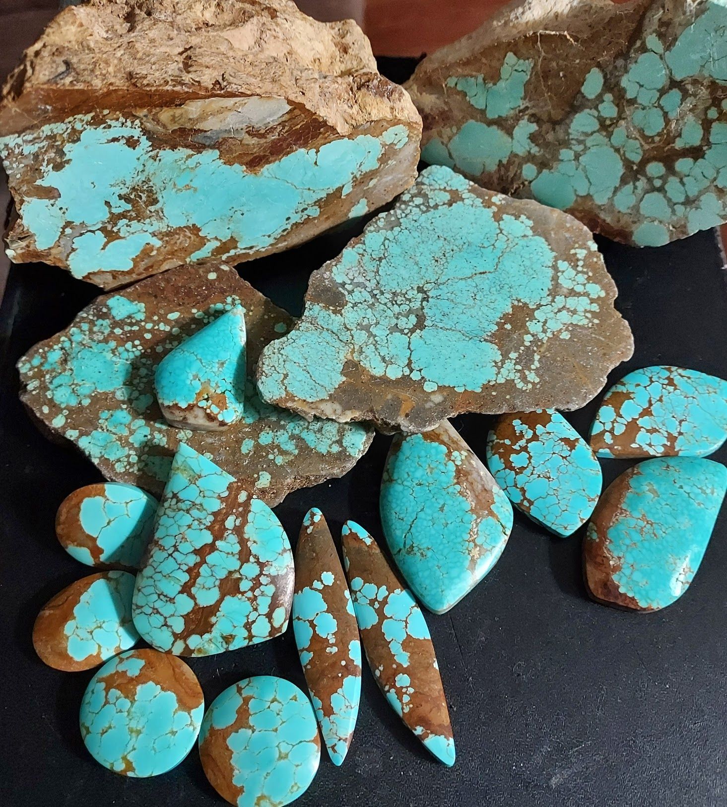 Turquoise stones with brown matrix, cut and uncut, various shapes, on a black surface.