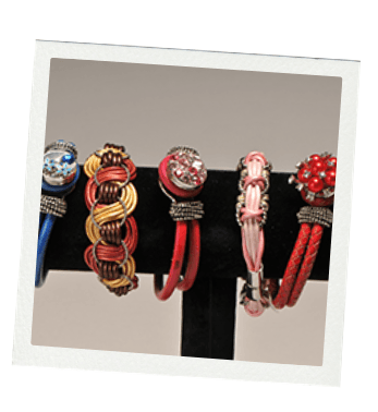 Five colorful leather and beaded bracelets on a black display stand.