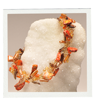 Orange and gold beaded necklace with gemstone pieces on a white, textured surface.