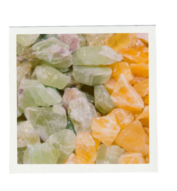Close-up of a pile of rough-cut gemstones in shades of green, yellow, and orange.