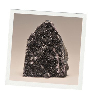 Dark, crystalline rock with white flecks, sitting on a neutral background, framed by a white border.