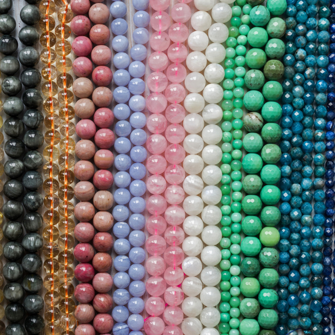 Rows of colorful gemstone beads in various colors, including shades of green, blue, pink, and brown.