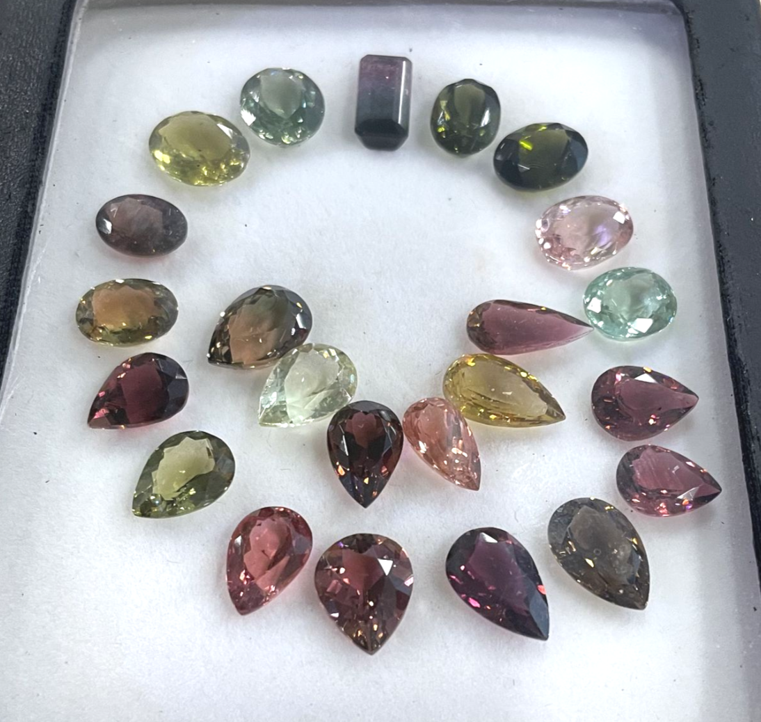 Various colored gemstones arranged in a semi-circle on a white background. Shades include green, pink, and brown.