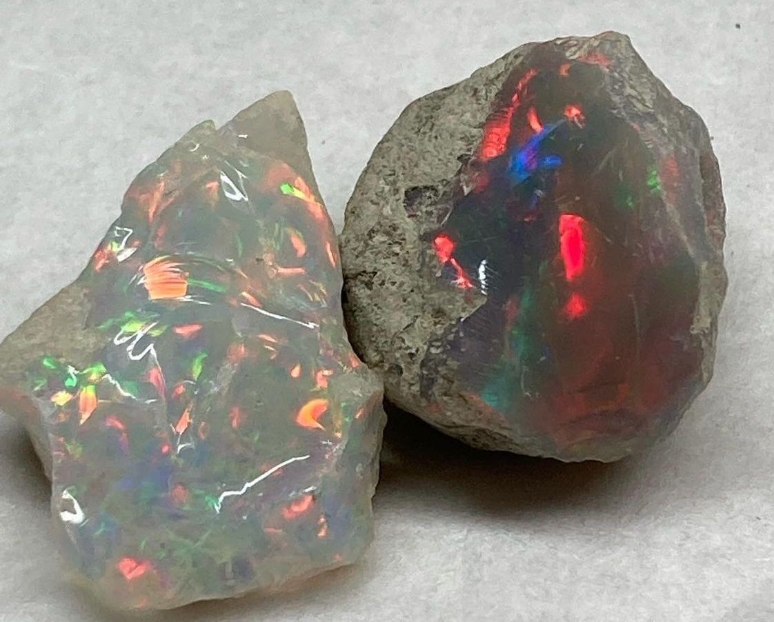 Two rough opals displaying vibrant play-of-color, with flashes of red, orange, and green.