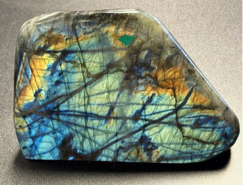 A polished labradorite gemstone, showing vibrant blue, gold, and green iridescence with dark crack-like inclusions.