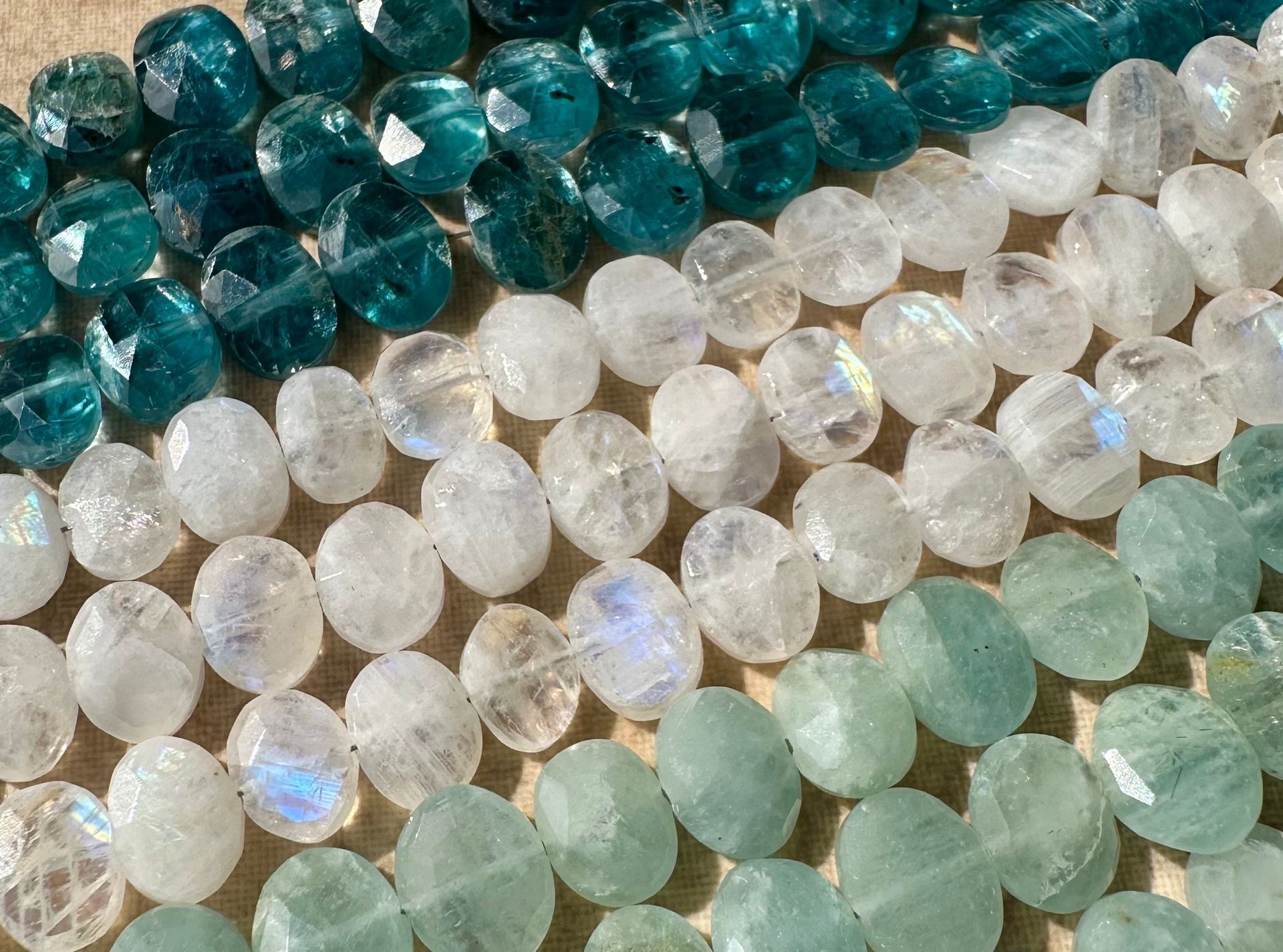 Rows of faceted gemstone beads in shades of teal, white, and pale green.