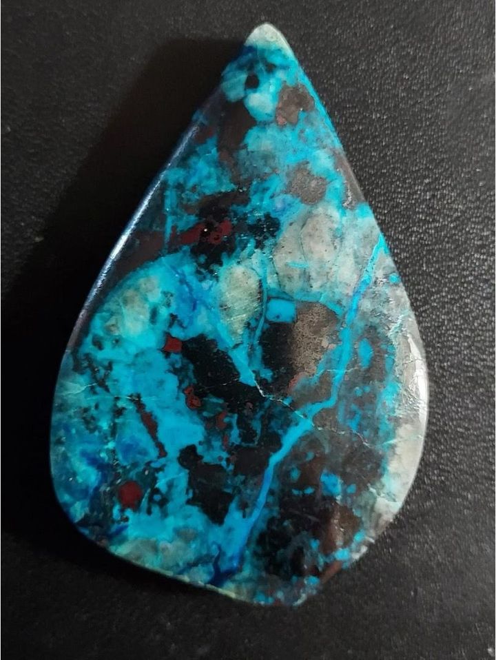 Teardrop-shaped polished gemstone with vibrant blue, black, and red inclusions.