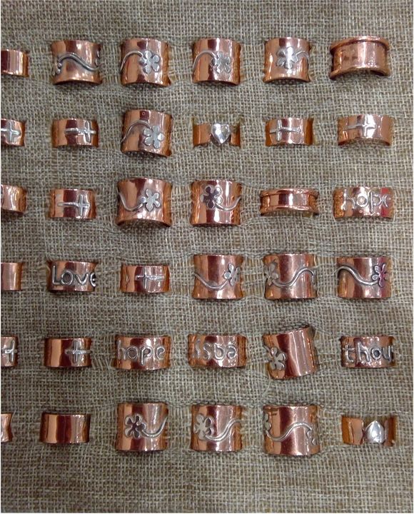 Rows of copper rings, some with silver designs, displayed on a textured surface.