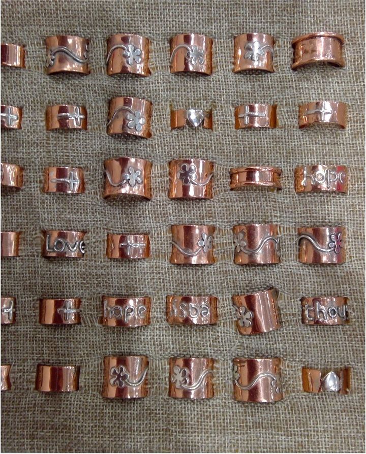 Rows of copper rings, some with silver designs, displayed on a textured surface.