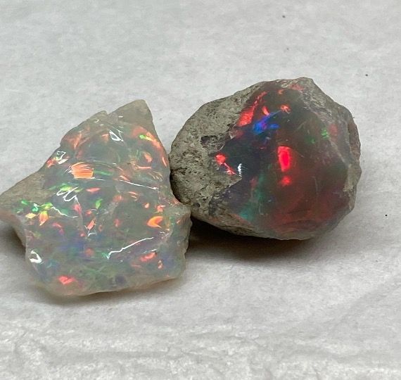 Two rough opals with vibrant flashes of color. One is primarily white, the other gray.