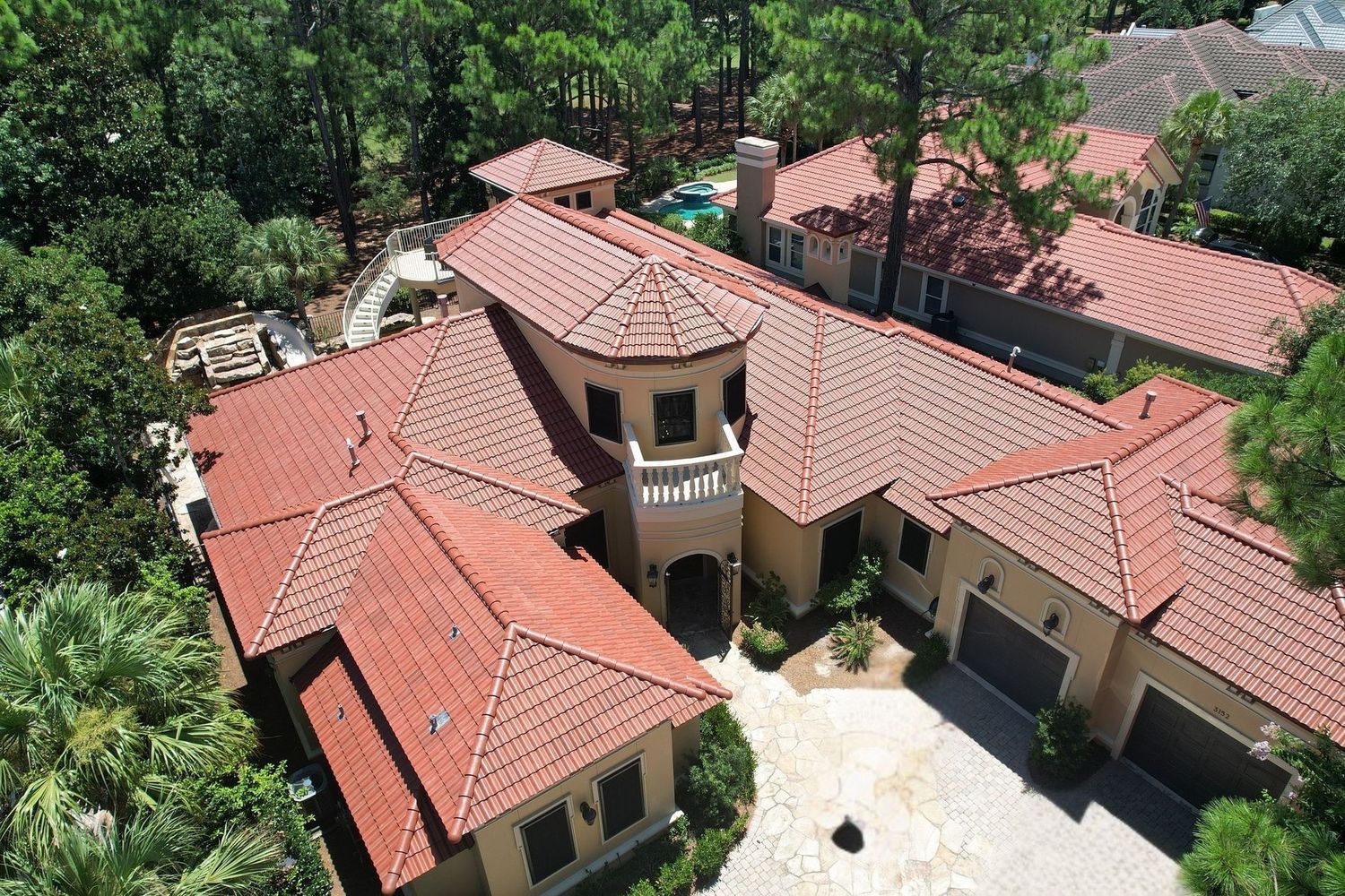 Aerial view of a large house with red-tiled roofs surrounded by trees and a courtyard