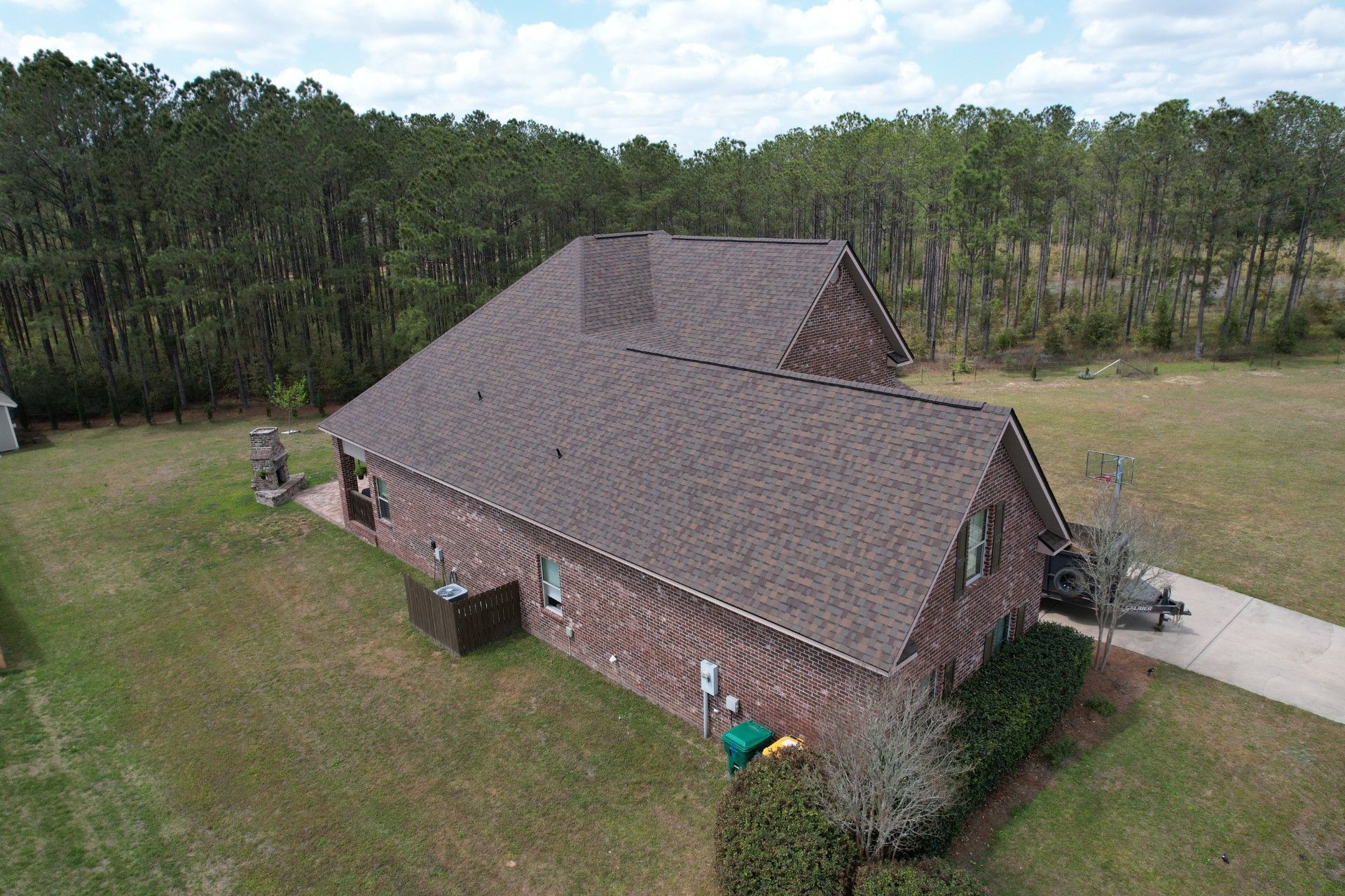 Aerial view of a brick house with a steep shingled roof, surrounded by grass and trees.