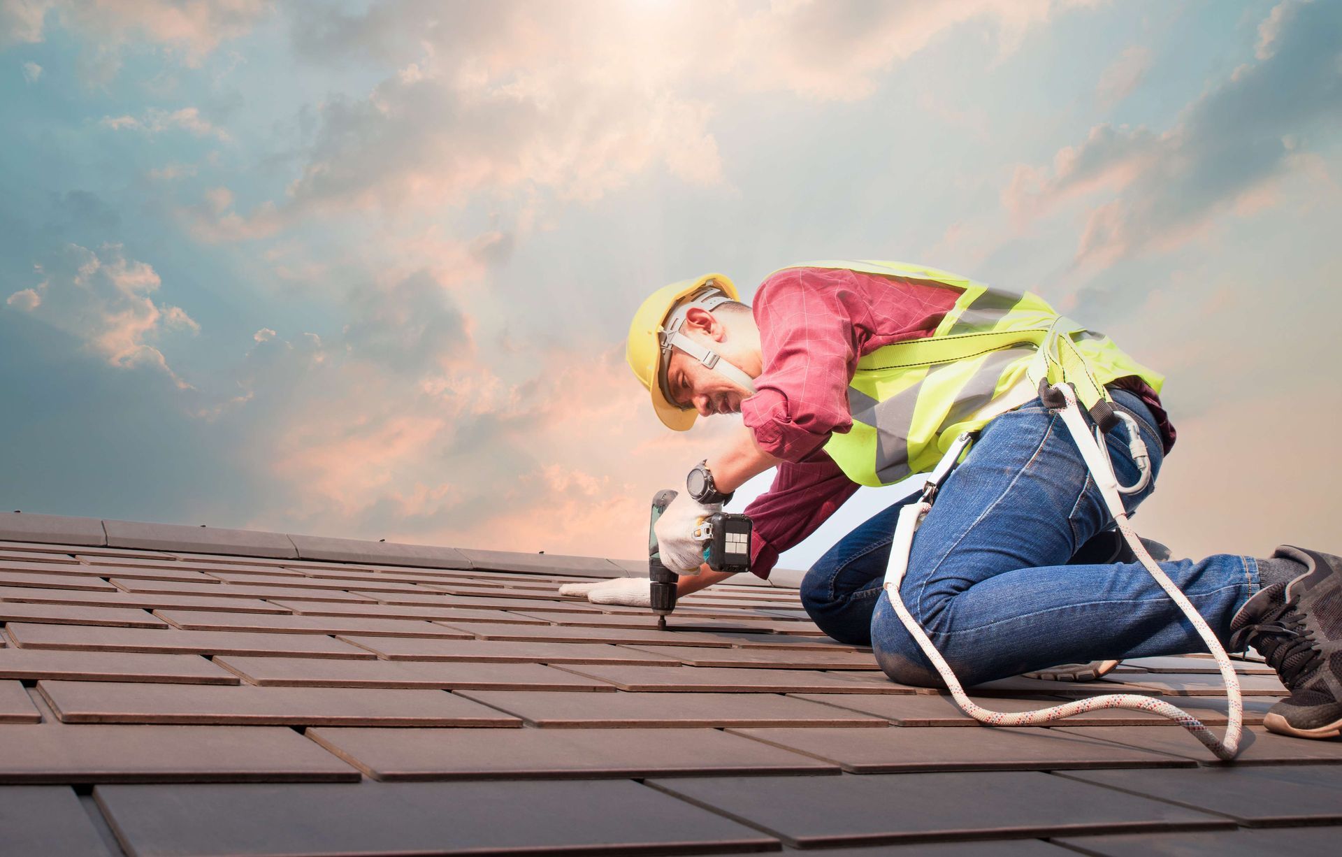 A dedicated roofing contractor using a power drill to secure tiles on a residential roof project. A dedicated roofing contractor using a power drill to secure tiles on a residential roof project.