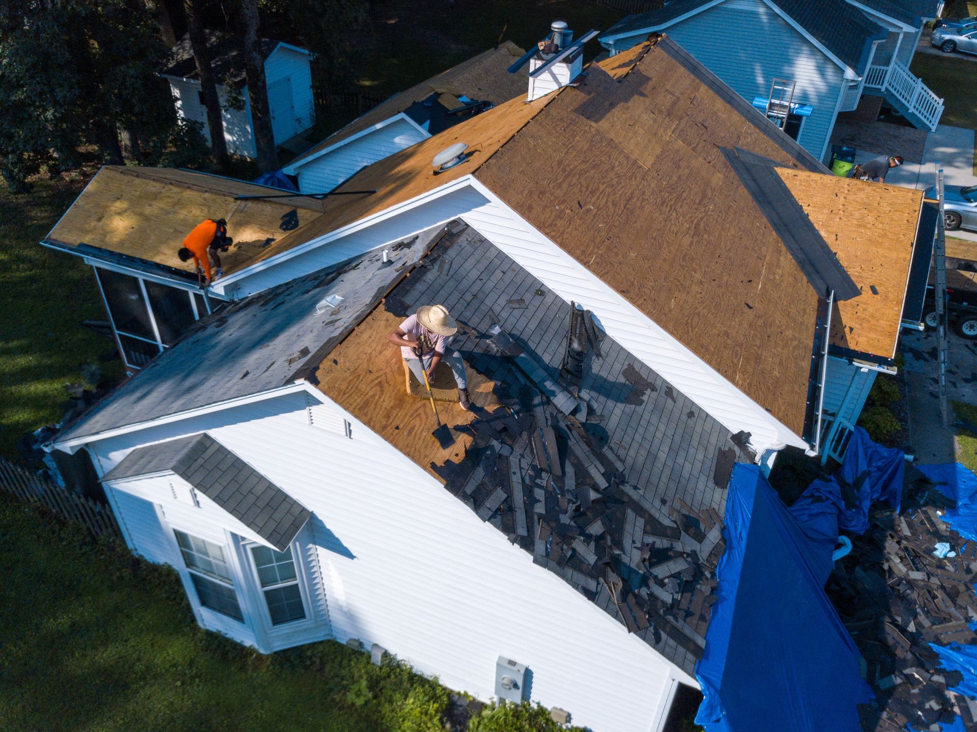 Aerial view of workers removing old shingles and replacing a house roof with new materials.