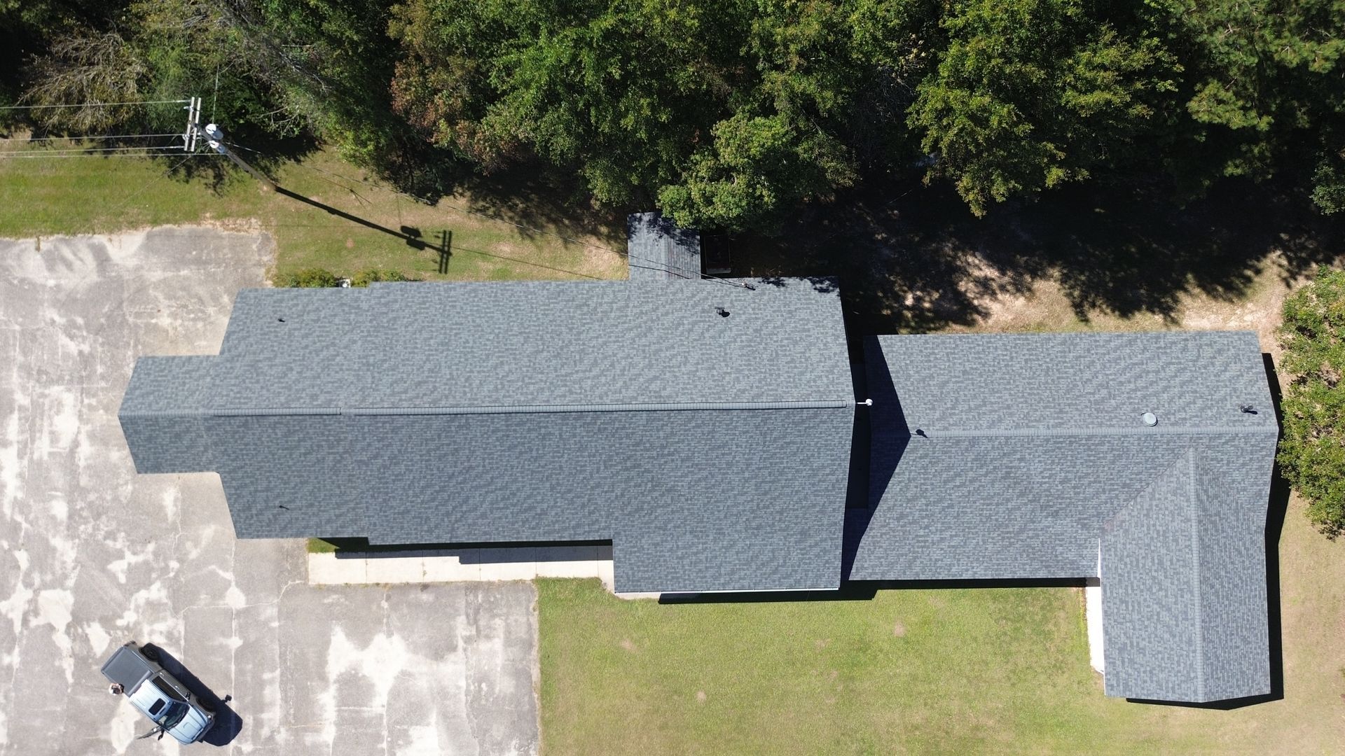 Aerial view of a gray-roofed house with a driveway, lawn, and trees surrounding it.