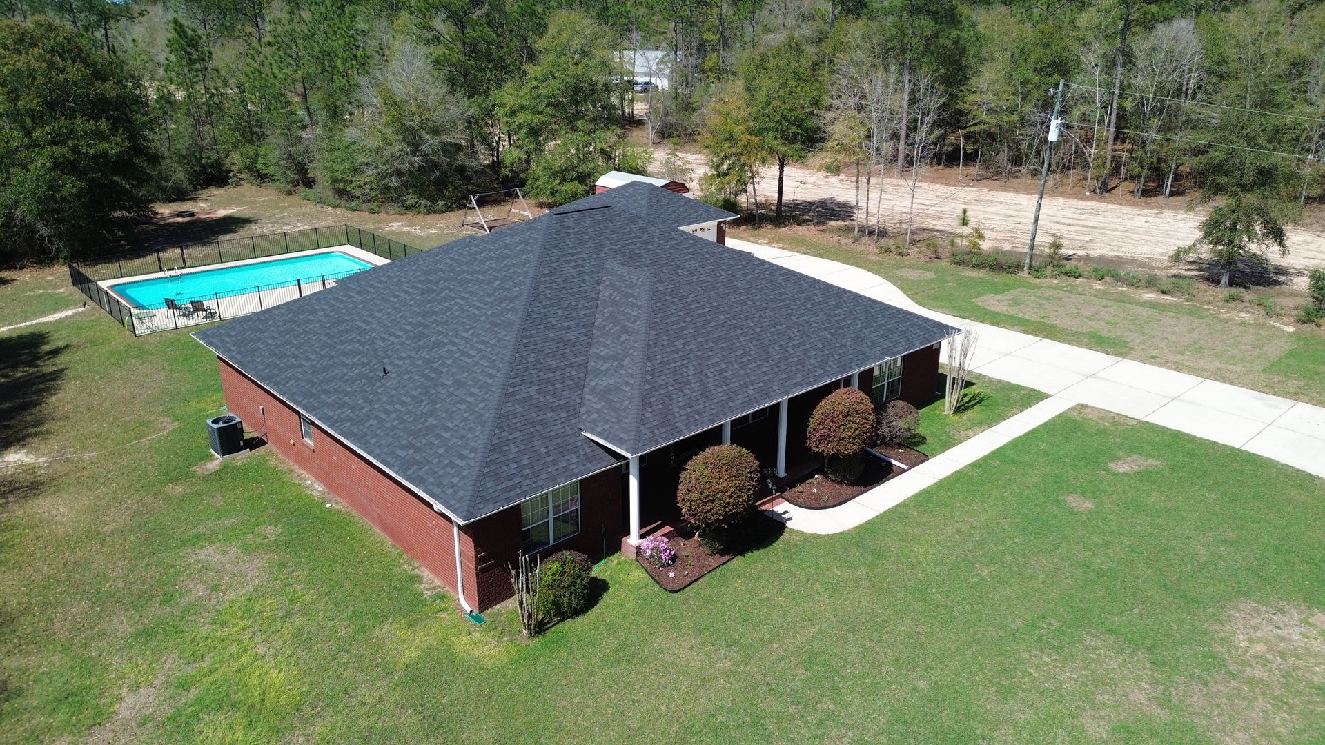 Aerial view of a red house with a dark roof, lawn, driveway, and a backyard swimming pool.