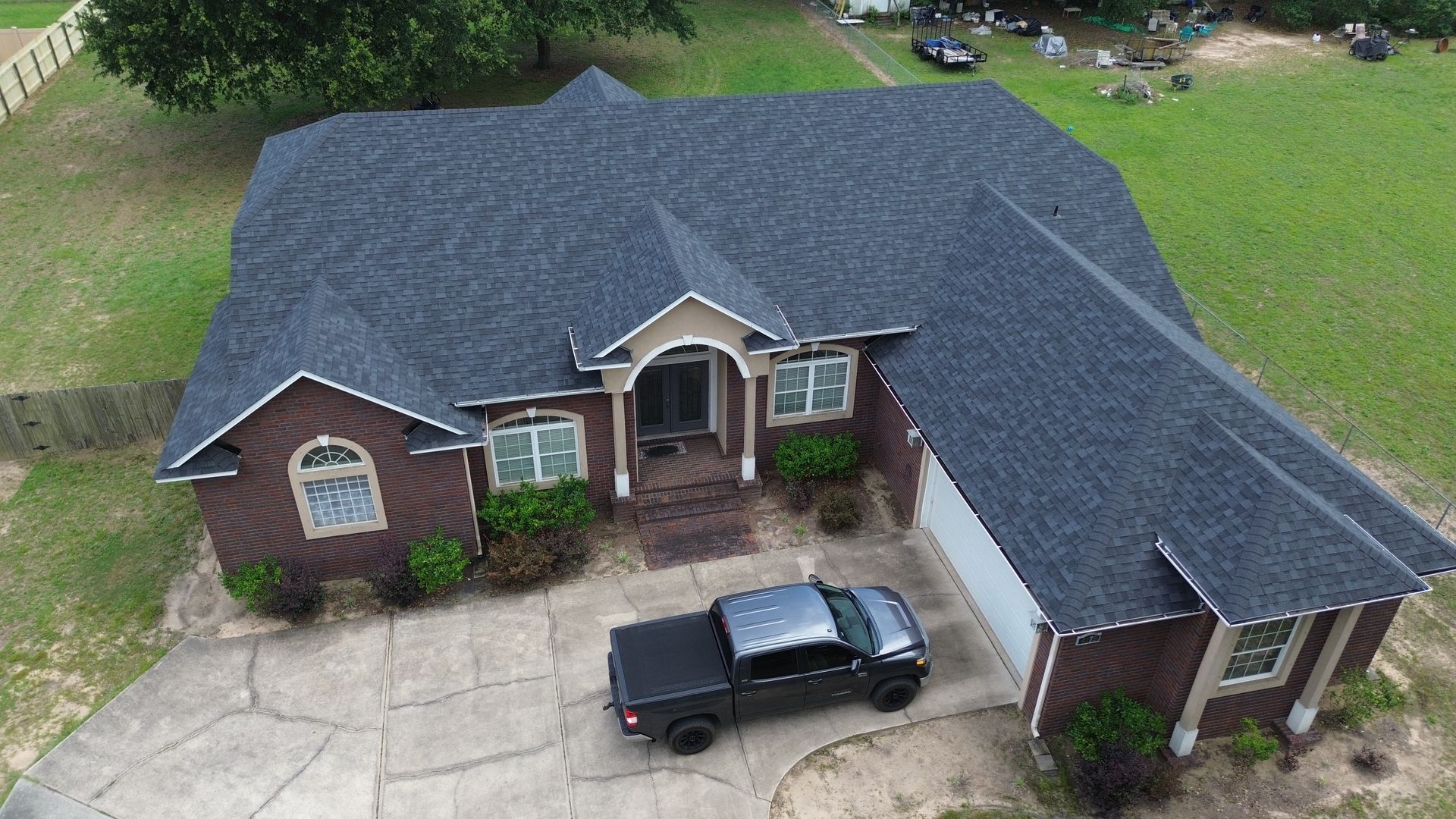 Aerial view of a brick house with a dark shingled roof and a black pickup truck in the driveway